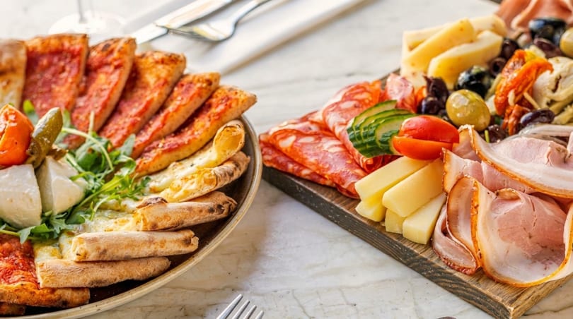 A plate of pizza slices and a charcuterie board with meats, cheeses, and olives.