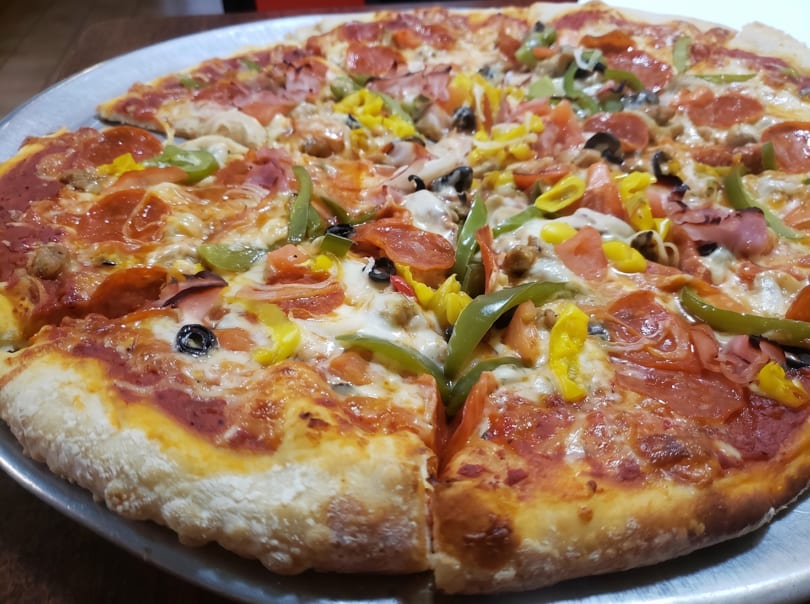 A large, freshly baked pizza with various toppings including pepperoni, ham, peppers, and olives.